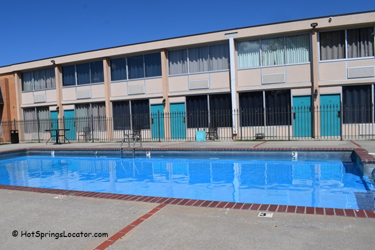 Hot Springs Hotel and Spa in Thermopolis Wyoming Hot Springs: A view of the hotel's outdoor swimming pool area with clear blue water, surrounded by several lounge chairs and umbrellas.