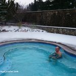 Bonneville Hot Springs Resort WA Washington: A person relaxing in a steaming outdoor hot tub, surrounded by snow-covered ground and stone walls, with evergreen trees in the background.