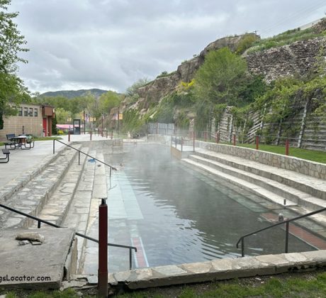 Lava Hot Springs Foundation World Famous Hot Springs Idaho: The picture "Lava Hot Springs Foundation World Famous Hot Springs Idaho main pool with stone steps" presents a large rectangular hot spring pool with steam rising, flanked by wide stone steps and retaining walls, with rocky hills and greenery in the background.