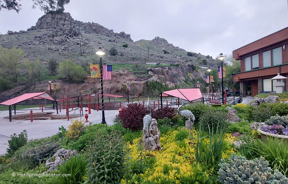 Lava Hot Springs Foundation World Famous Hot Springs Idaho: The picture "Lava Hot Springs Foundation World Famous Hot Springs Idaho garden and pools" features landscaped gardens with flowering plants and decorative sculptures, and red-roofed pool shelters with rocky hills in the background.