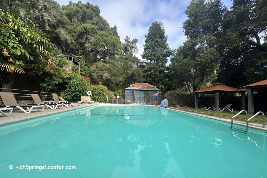 Sycamore Mineral Springs Resort & Spa California: The picture "Sycamore Mineral Springs Resort & Spa California swimming pool" features a large outdoor pool surrounded by lounge chairs and shaded cabanas, with lush greenery and a small building with a red tile roof at the far end.