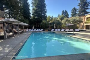 Fairmont Sonoma Mission Inn & Spa in California: The picture "Fairmont Sonoma Mission Inn & Spa in California spa pool with loungers" displays a tranquil outdoor pool area lined with white-cushioned lounge chairs and umbrellas, set among trees and greenery for a relaxing atmosphere.