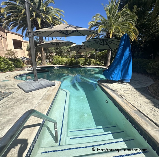 Fairmont Sonoma Mission Inn & Spa in California: The picture "Fairmont Sonoma Mission Inn & Spa in California outdoor whirlpool" shows a curving outdoor hot tub with steps and handrails, shaded by large umbrellas and surrounded by palm trees and lush gardens.