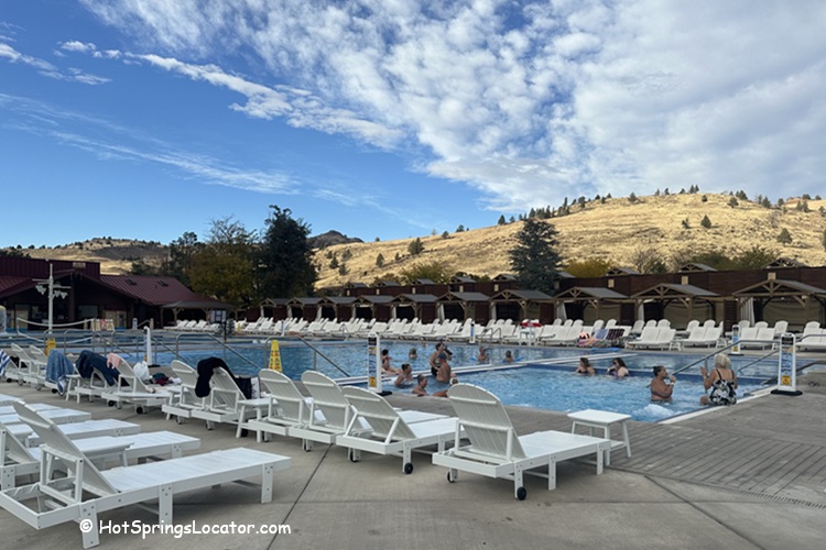 Kah-Nee-Ta Resort and Spa in Idaho: The picture "Kah-Nee-Ta Resort and Spa in Oregon outdoor swimming pool with lounge chairs and hills" shows people relaxing in a large outdoor swimming pool, surrounded by white lounge chairs and cabanas, with rolling golden hills and a partly cloudy sky in the background.