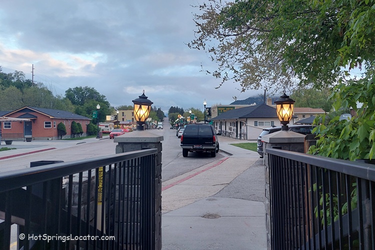 The City of Lava Hot Springs in Idaho: The picture "downtown street view at dusk" features a view looking down a small-town street lined with homes and businesses, with warm street lamps lighting the sidewalk and parked cars visible in the early evening light.