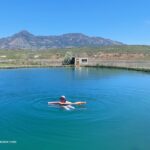 Belmont Hot Springs (Formerly Udy Hot Springs): Utah's Geothermal Resort in northern Utah - Floating in Belmont Hot Springs Floating in Belmont Hot Springs features a person relaxing on a pool noodle in the calm, blue geothermal pond, with a scenic mountain range and open sagebrush landscape in the background.
