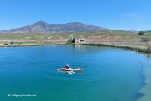 Belmont Hot Springs (Formerly Udy Hot Springs): Utah's Geothermal Resort in northern Utah - Floating in Belmont Hot Springs Floating in Belmont Hot Springs features a person relaxing on a pool noodle in the calm, blue geothermal pond, with a scenic mountain range and open sagebrush landscape in the background.