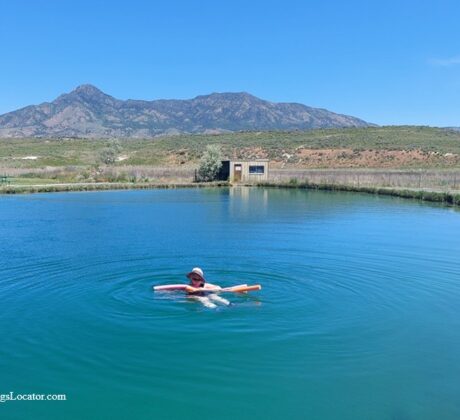 Belmont Hot Springs (Formerly Udy Hot Springs): Utah's Geothermal Resort in northern Utah - Floating in Belmont Hot Springs Floating in Belmont Hot Springs features a person relaxing on a pool noodle in the calm, blue geothermal pond, with a scenic mountain range and open sagebrush landscape in the background.