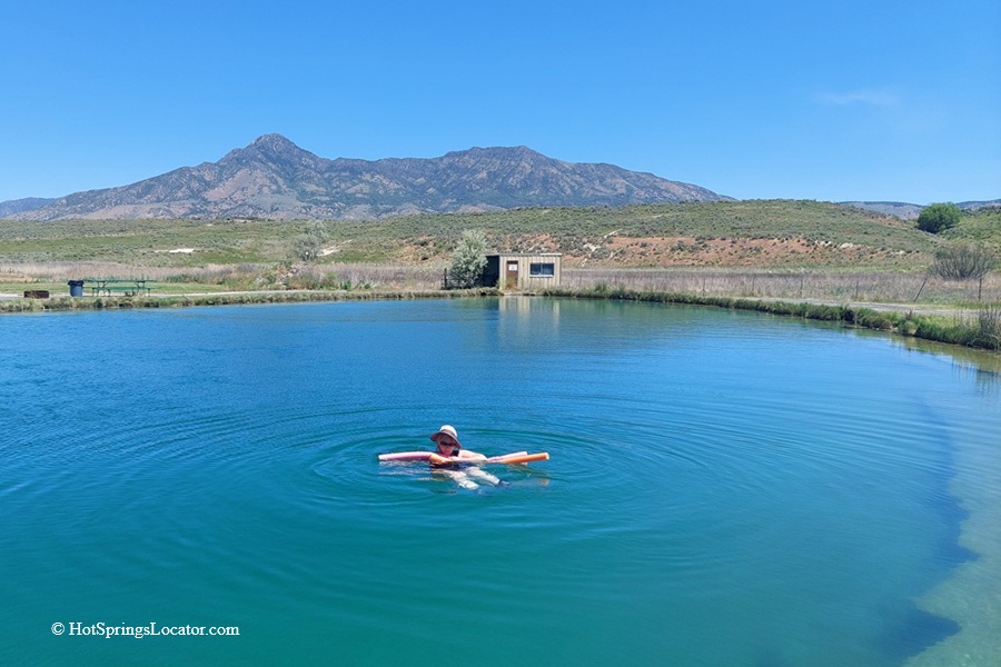 Belmont Hot Springs (Formerly Udy Hot Springs): Utah's Geothermal Resort in northern Utah - Floating in Belmont Hot Springs Floating in Belmont Hot Springs features a person relaxing on a pool noodle in the calm, blue geothermal pond, with a scenic mountain range and open sagebrush landscape in the background.