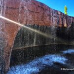 Crystal Hot Springs in Utah - Waterfall at Crystal Hot Springs Crystal Hot Springs in Utah: The picture "Waterfall at Crystal Hot Springs" captures a close-up of the hot spring’s artificial red rock wall with steaming water cascading down into the pool below, where a swimmer enjoys the falls.