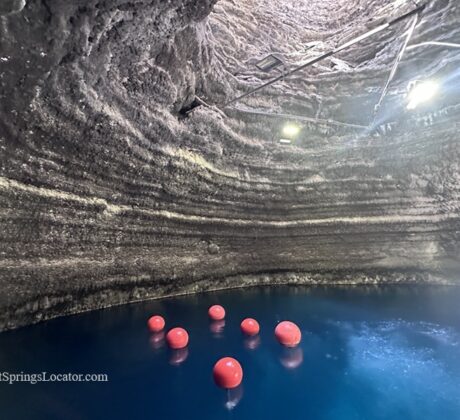 Homestead Crater Hot Springs in Utah: The picture "Homestead Crater Interior" displays the inside of the natural dome-shaped crater with blue mineral water and several floating red buoys, illuminated by overhead lights attached to the rock walls.