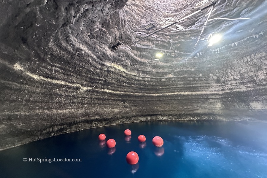 Homestead Crater Hot Springs in Utah: The picture "Homestead Crater Interior" displays the inside of the natural dome-shaped crater with blue mineral water and several floating red buoys, illuminated by overhead lights attached to the rock walls.