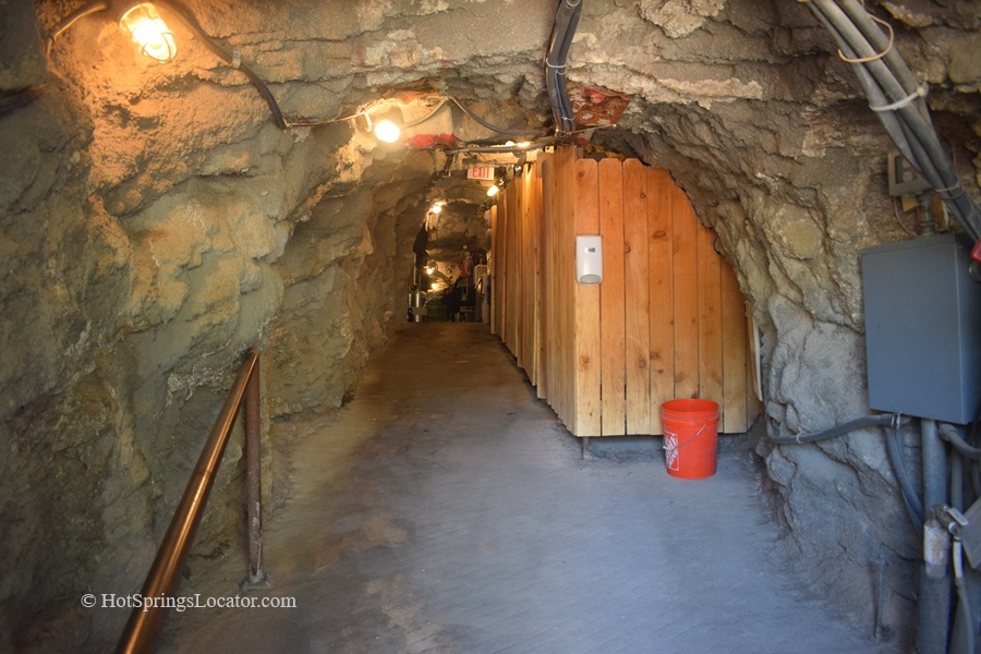 Homestead Crater Hot Springs in Utah: The picture "Homestead Crater Tunnel" features a lit tunnel carved through rock, with wooden changing stalls on the right and utility pipes running along the wall, forming the entrance to the hot springs.