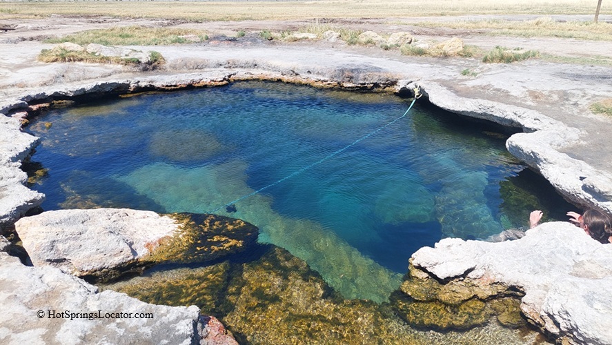 Meadow Hot Springs in Utah: The picture "Meadow Hot Springs Water Close-up" shows a close-up of the crystal-clear blue water in the hot springs, surrounded by rocky ledges, with a partially submerged rope leading into the pool and a person relaxing at the edge.