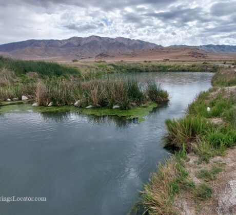 Horseshoe Springs in Utah – Horseshoe Springs Marsh View Horseshoe Springs in Utah – The picture "Horseshoe Springs Marsh View" shows a calm spring-fed pond surrounded by green reeds and grasses, with distant dry hills and rugged mountains under a cloudy sky.